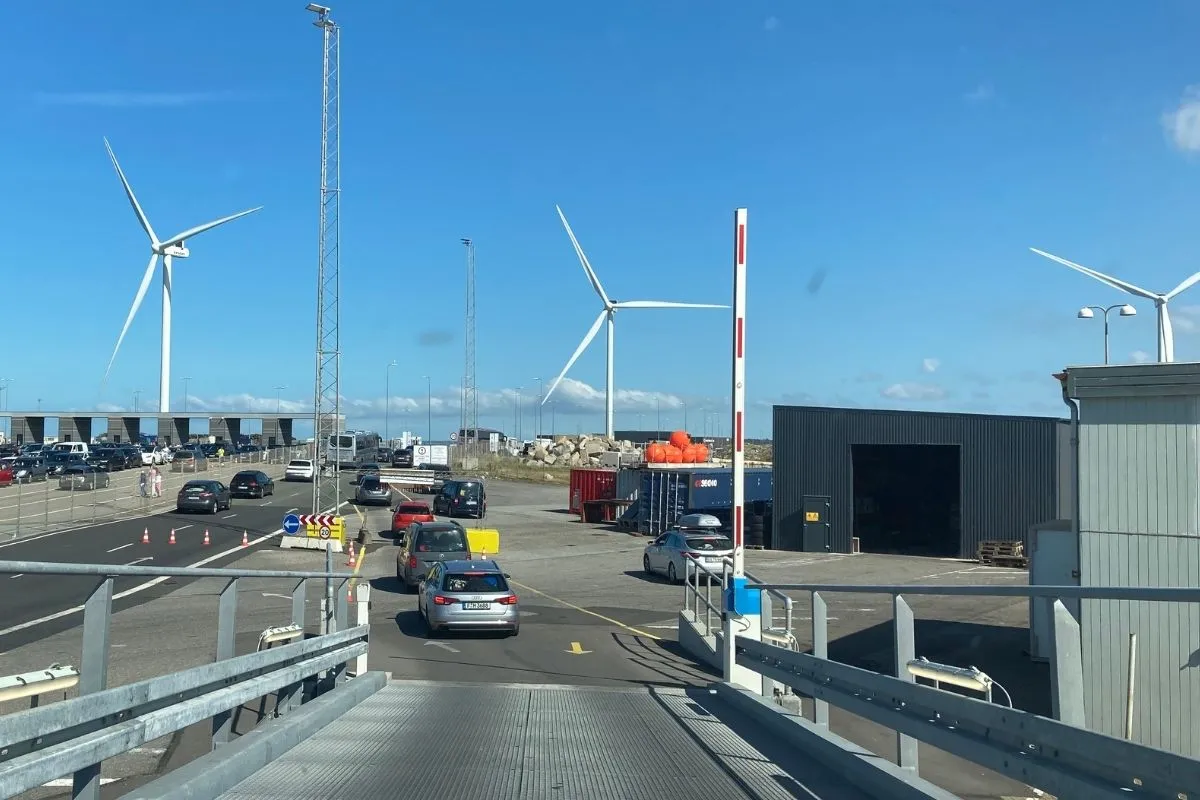 Cars driving off the ferry down the ramp, wind turbines behind the terminal