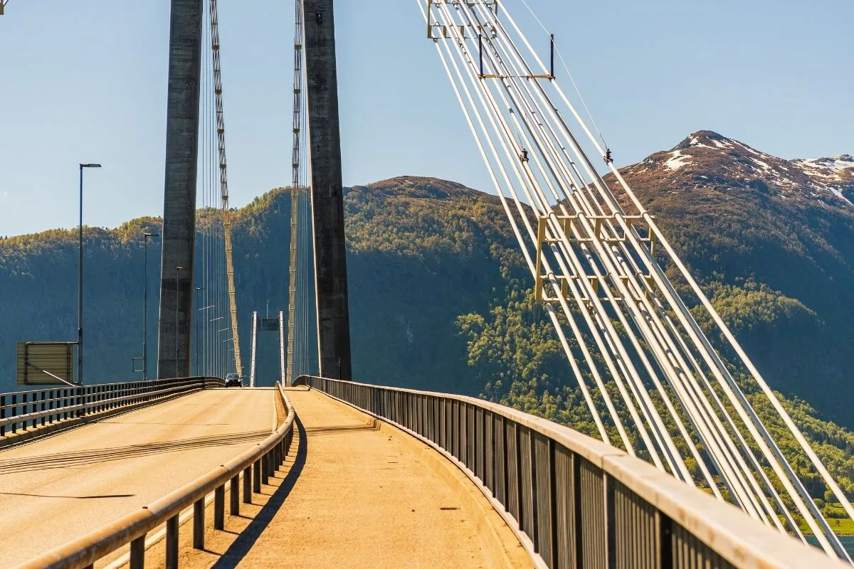 A suspension bridge carrying the road across a fjord, mountains behind