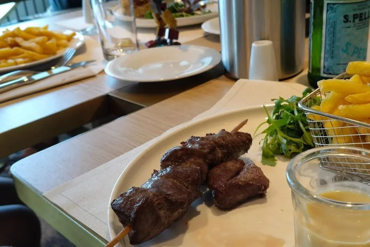 A meal on board: a skewer with fries and salad on a table by the window